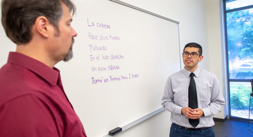 student and professor talking in front of white board with Spanish phrases