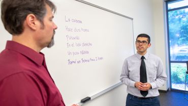 student and professor talking in front of white board with Spanish phrases